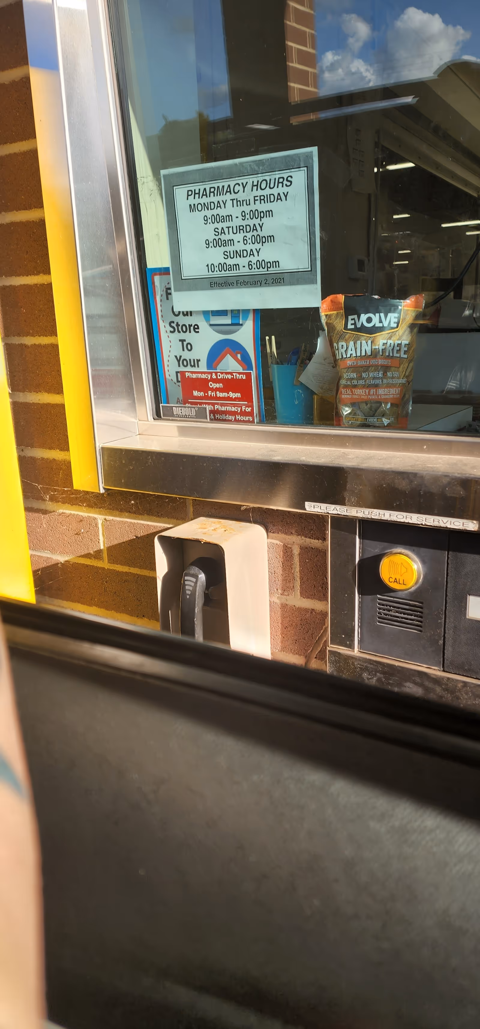 Drive-thru pharmacy window at Discount Drug Mart with posted hours sign
