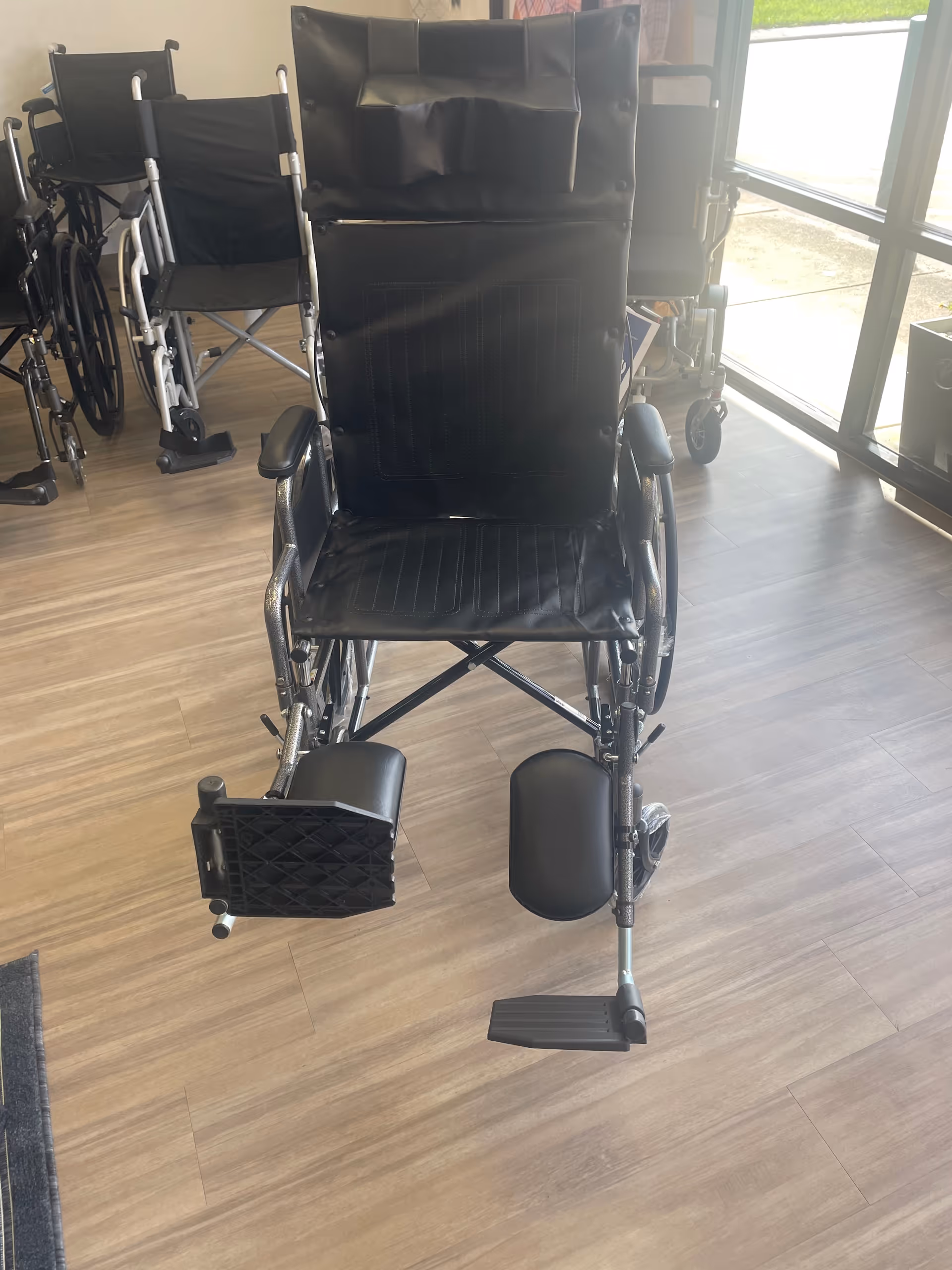 Front view of a black wheelchair in a BlueCare showroom with other wheelchairs nearby.