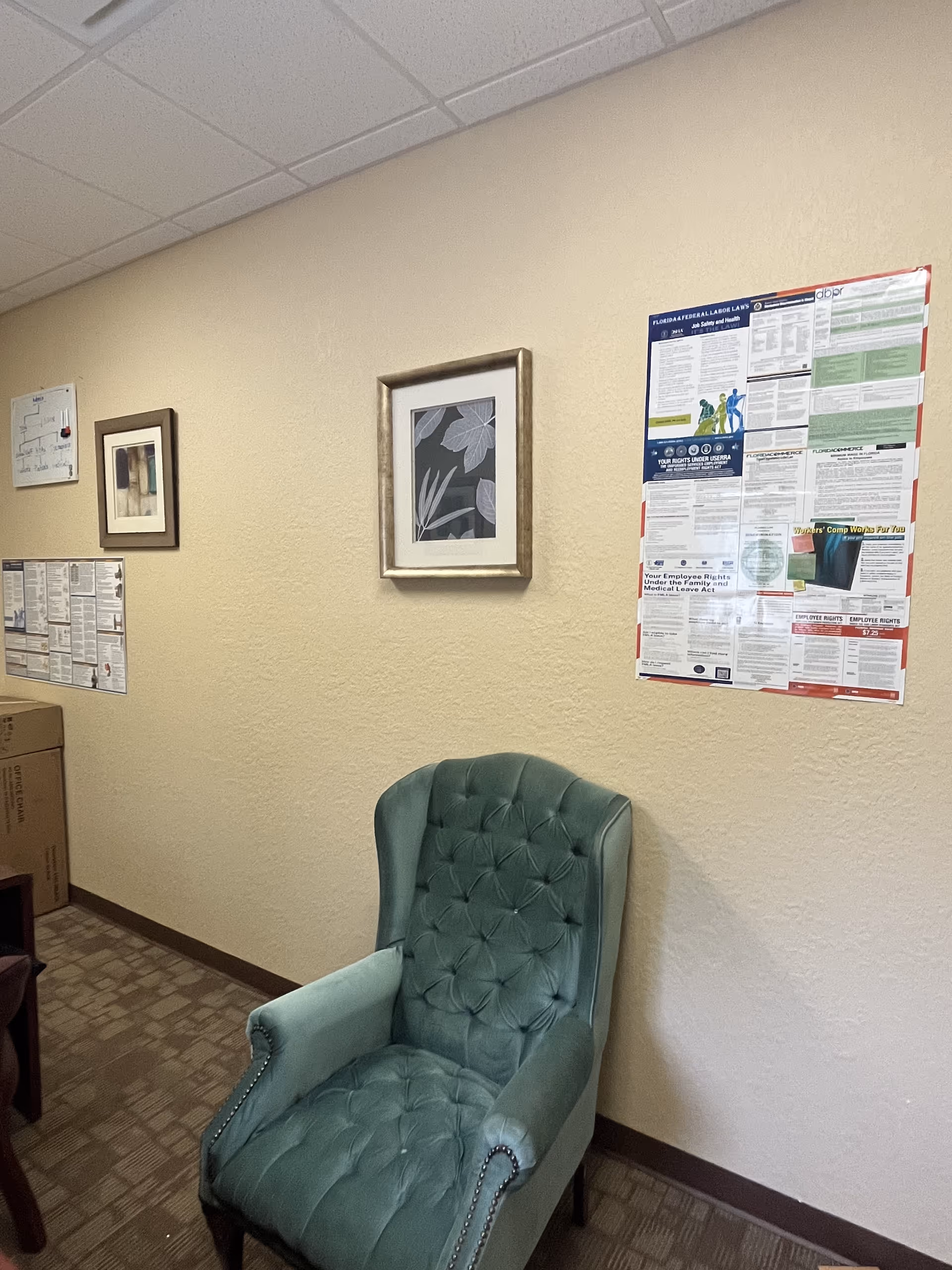 Teal tufted chair sits in a beige-walled hallway with framed art and posters.