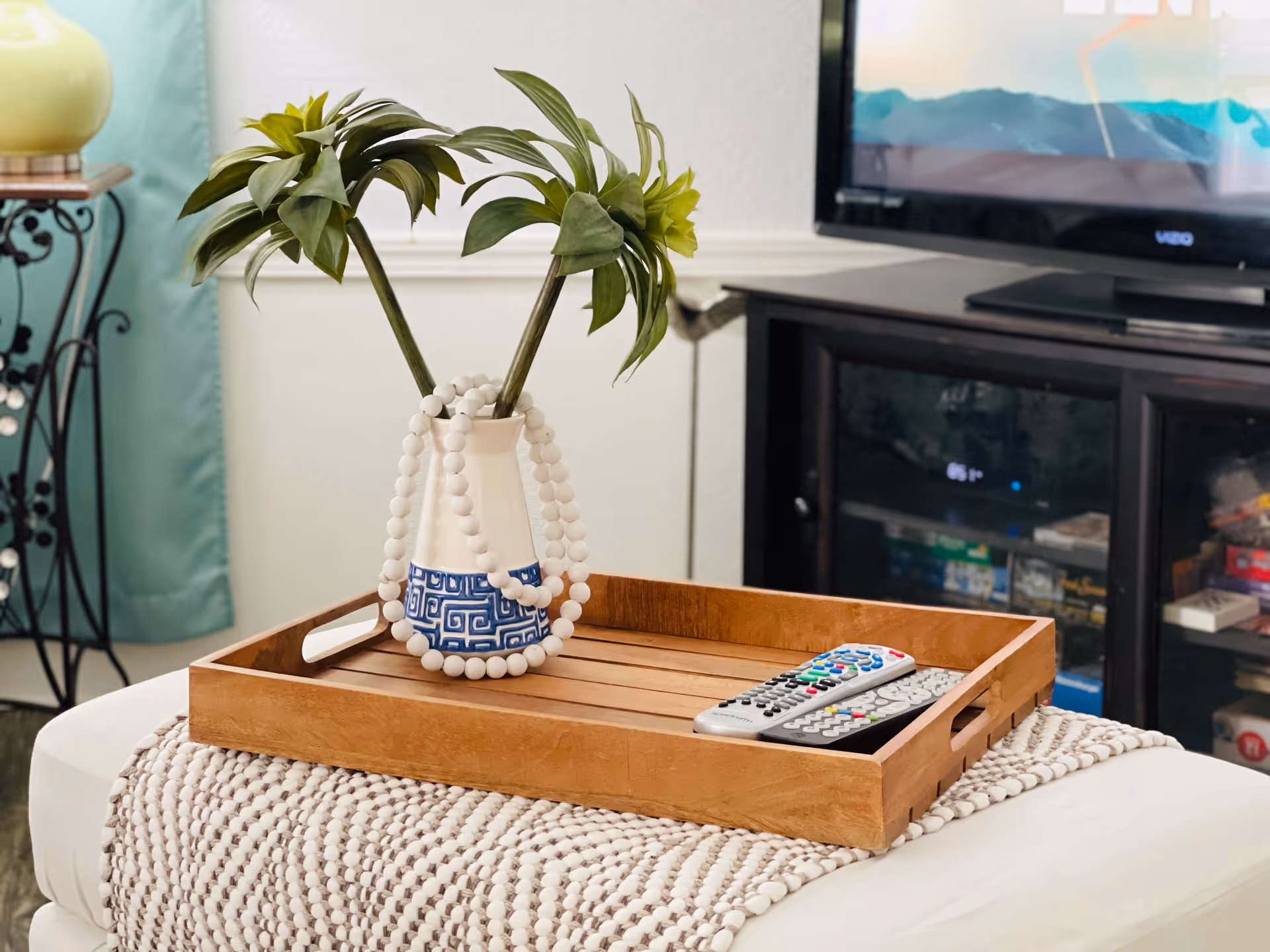 Wooden tray with a potted plant and beaded decor on a knitted throw, near a TV.