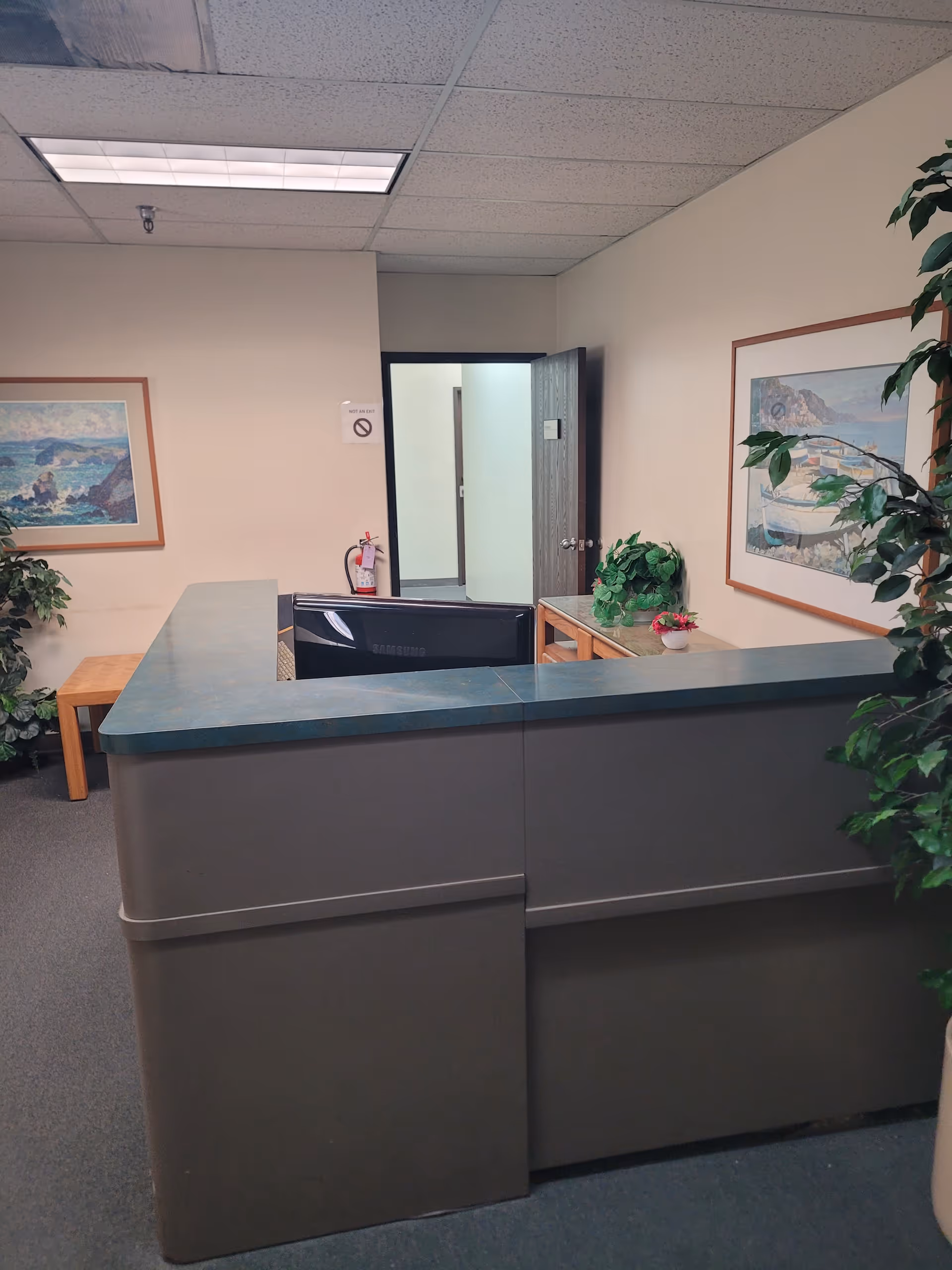 Lobby reception area with a curved counter, framed art, and potted plants.