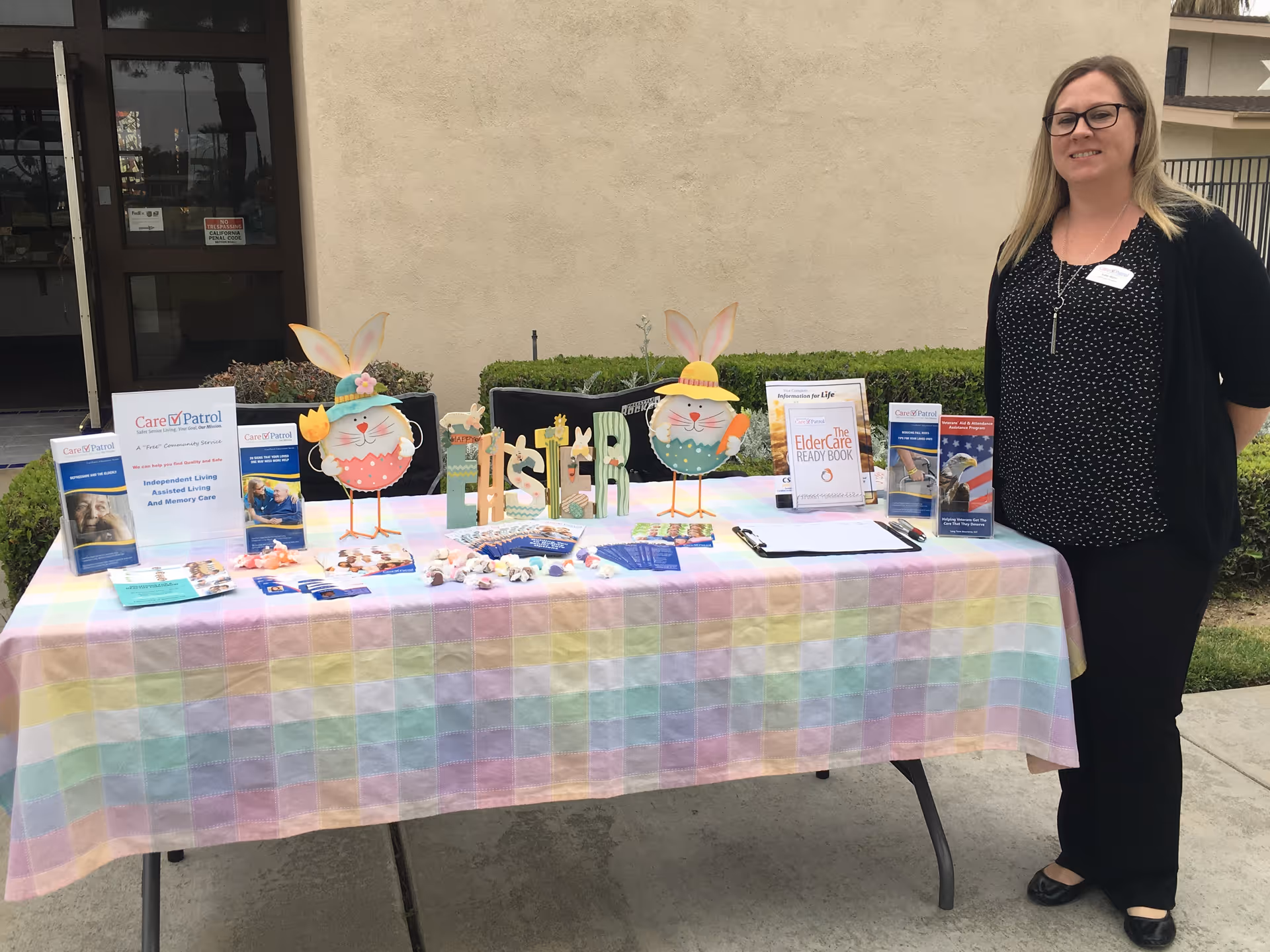 CarePatrol information table with brochures and Easter decorations outdoors beside a staff member.