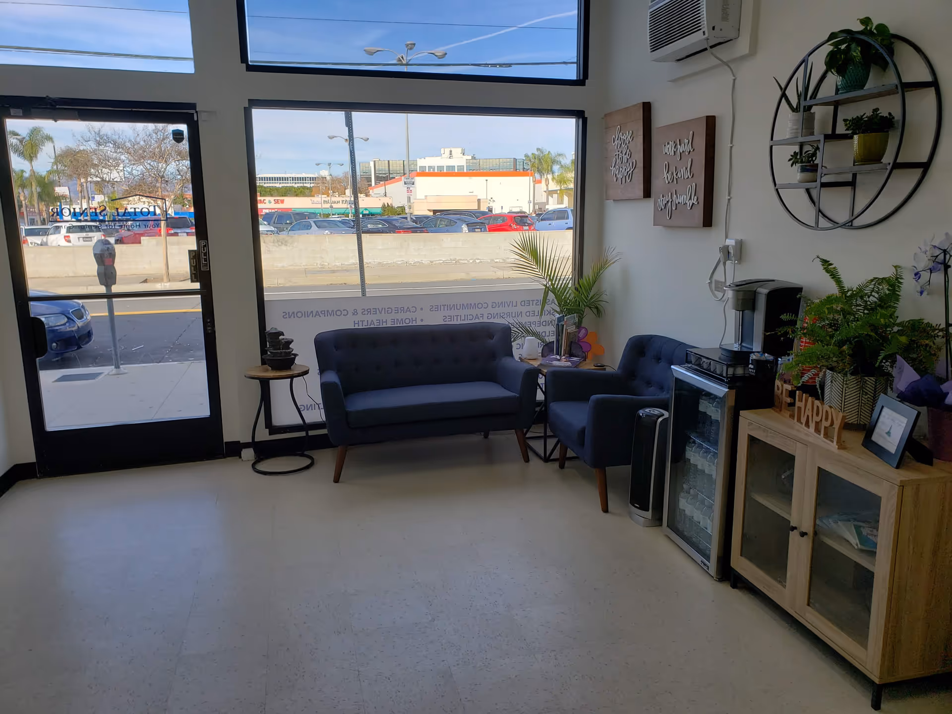 Lobby seating area with blue couches, plants, coffee station, and large front windows.
