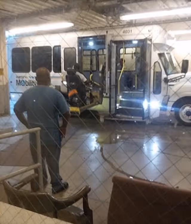 Man stands in a facility lobby as a wheelchair-accessible shuttle is parked outside.