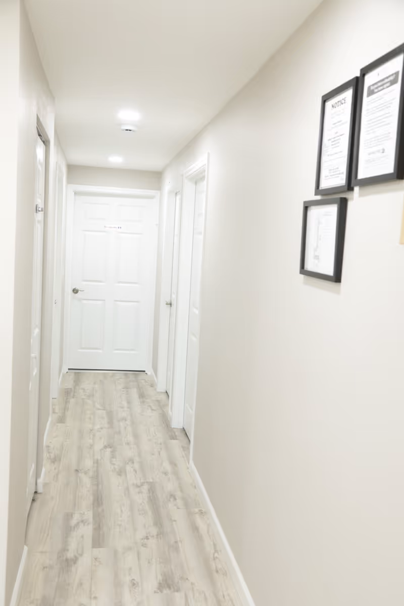 A bright white hallway with multiple doors and framed notices on the wall.