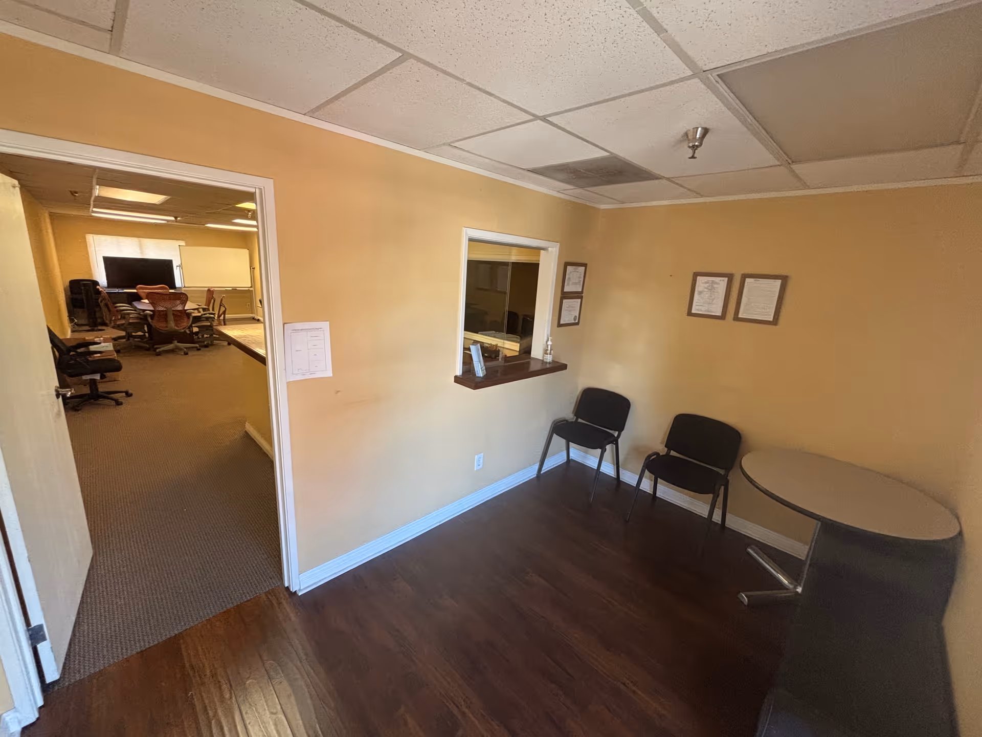 Waiting area with two chairs, round table, and service window leading to a meeting room.