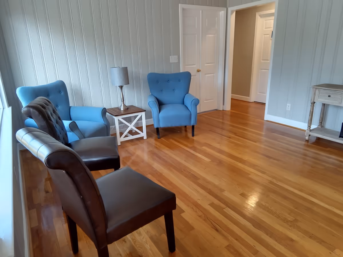 Bright living room with blue upholstered chairs, a small table, lamp, and wooden floors.