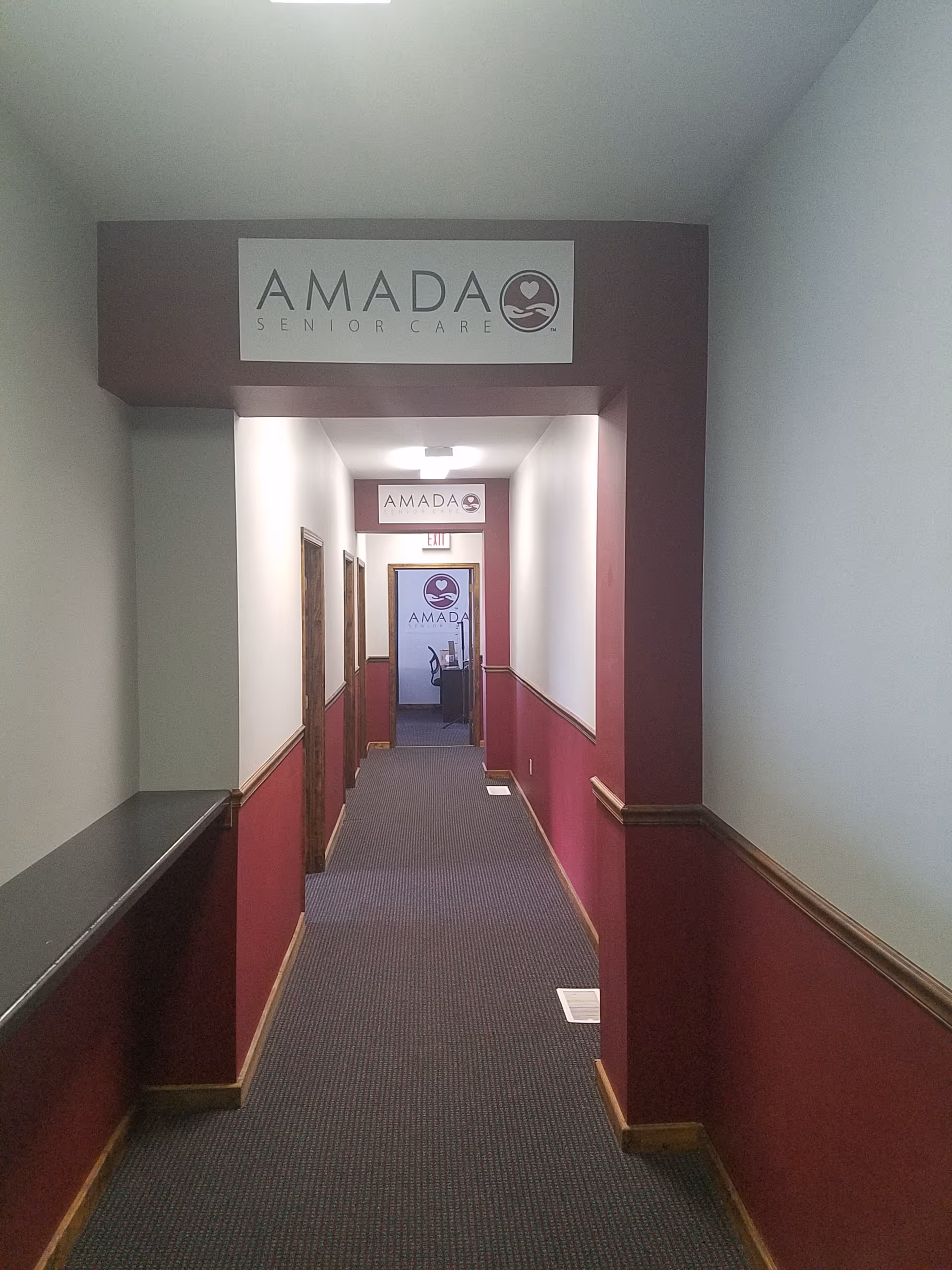 A long corridor in an Amada Senior Care facility with maroon walls and signs.
