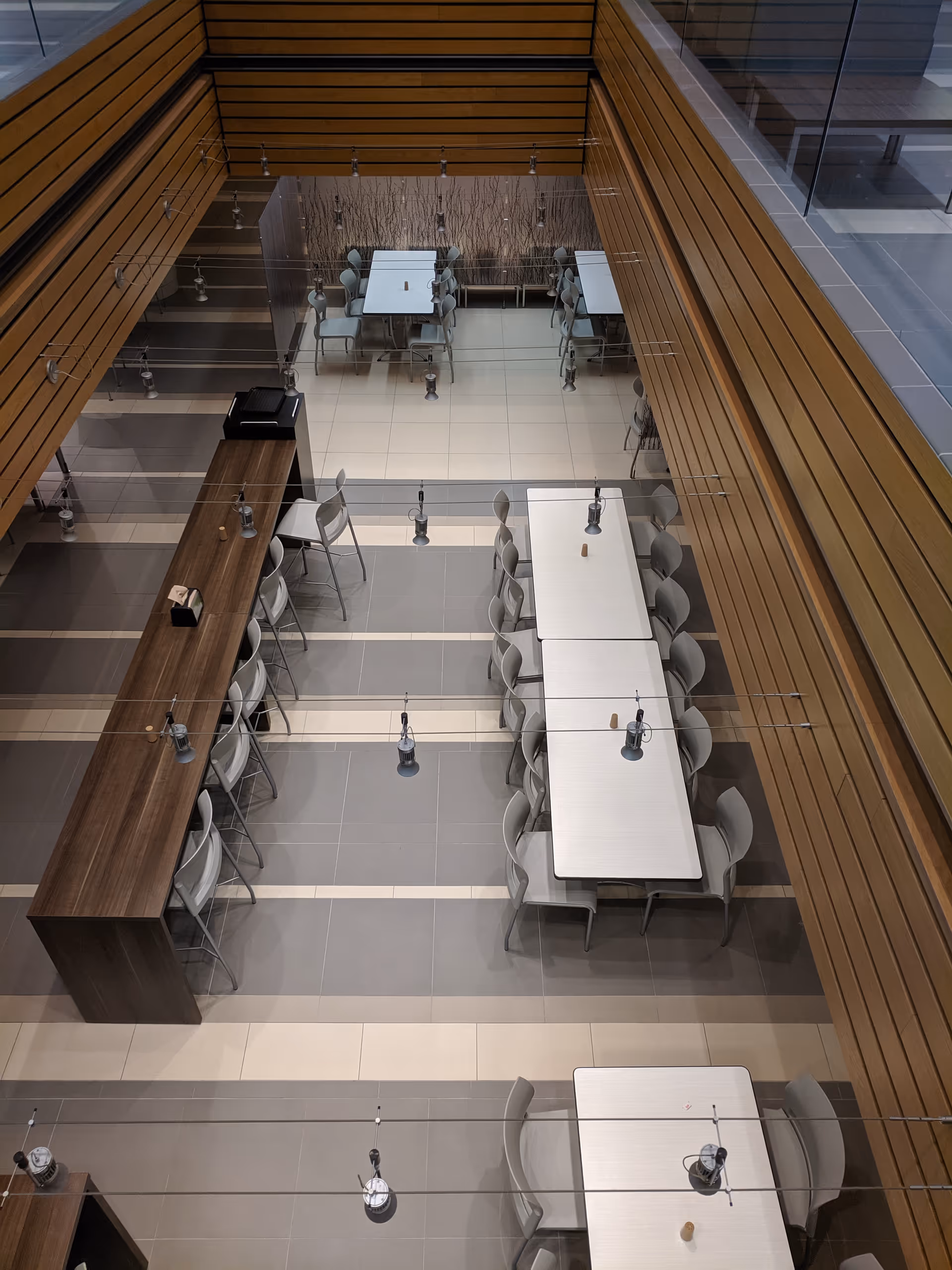 A multi-level interior dining area with long tables, chairs, and a wooden accent wall.