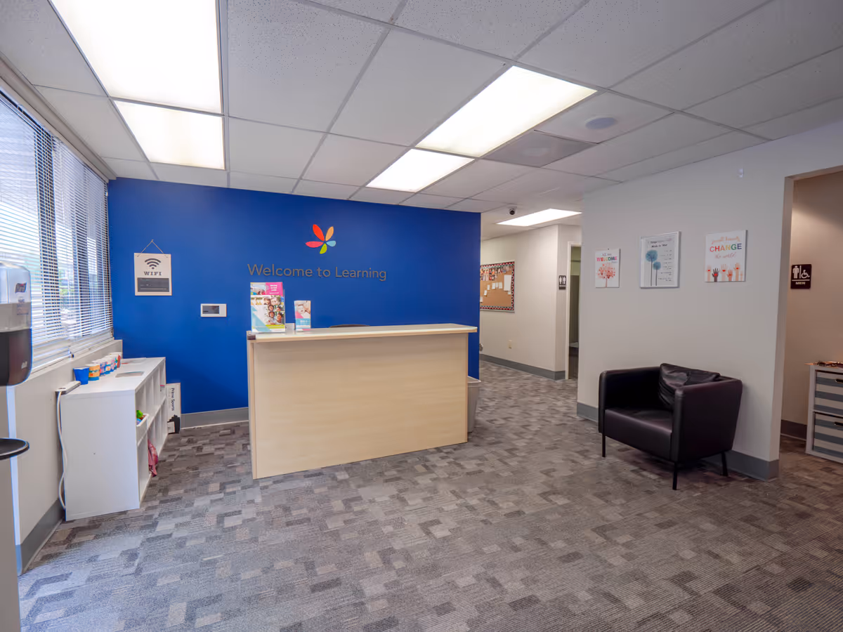 Reception area with a light wood front desk, blue learning wall, chairs, and posters.