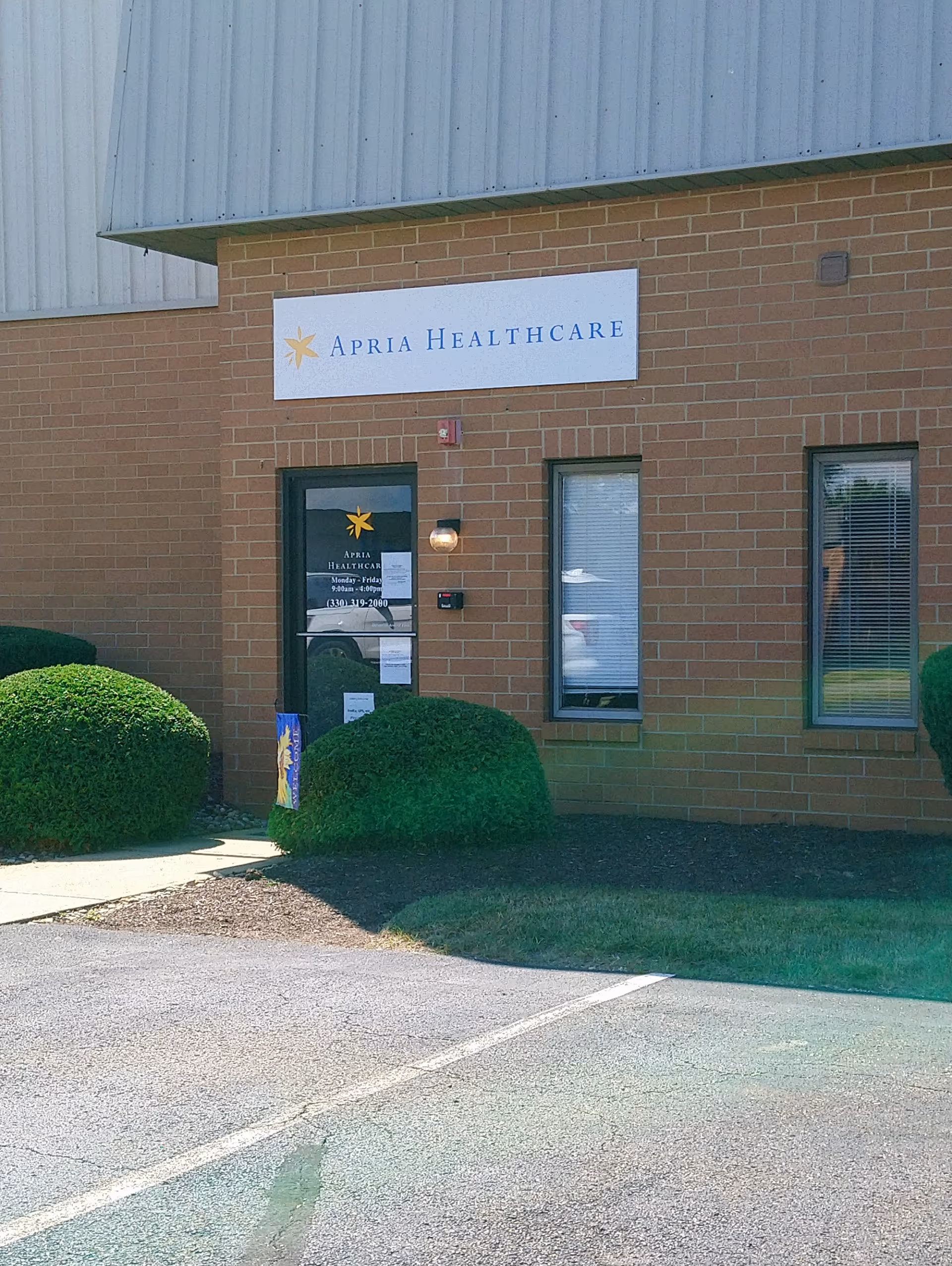 Brick building entrance with Apria Healthcare sign and trimmed shrubs.