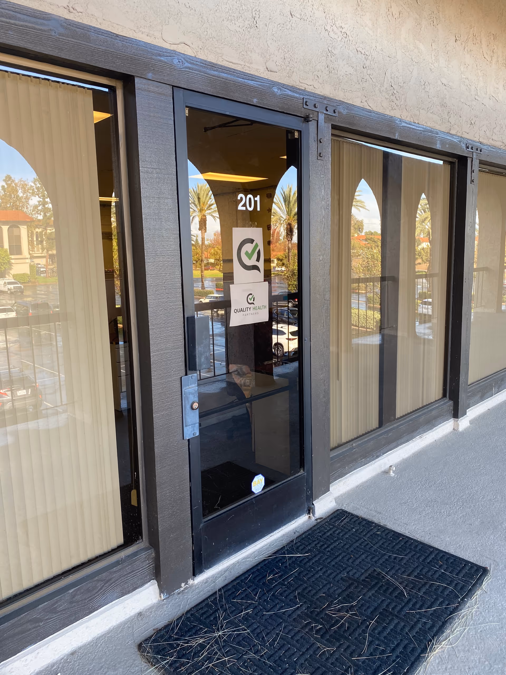 Glass entrance door of Quality Health Partners, unit 201, with exterior storefront and signage.
