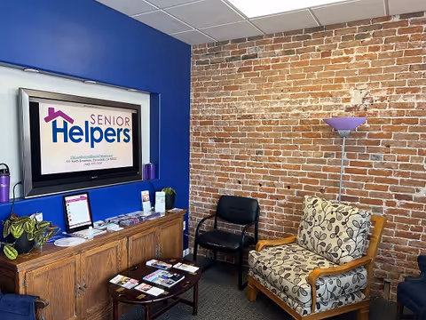A lounge area with brick wall, blue accent wall, TV, and seating in Senior Helpers facility.