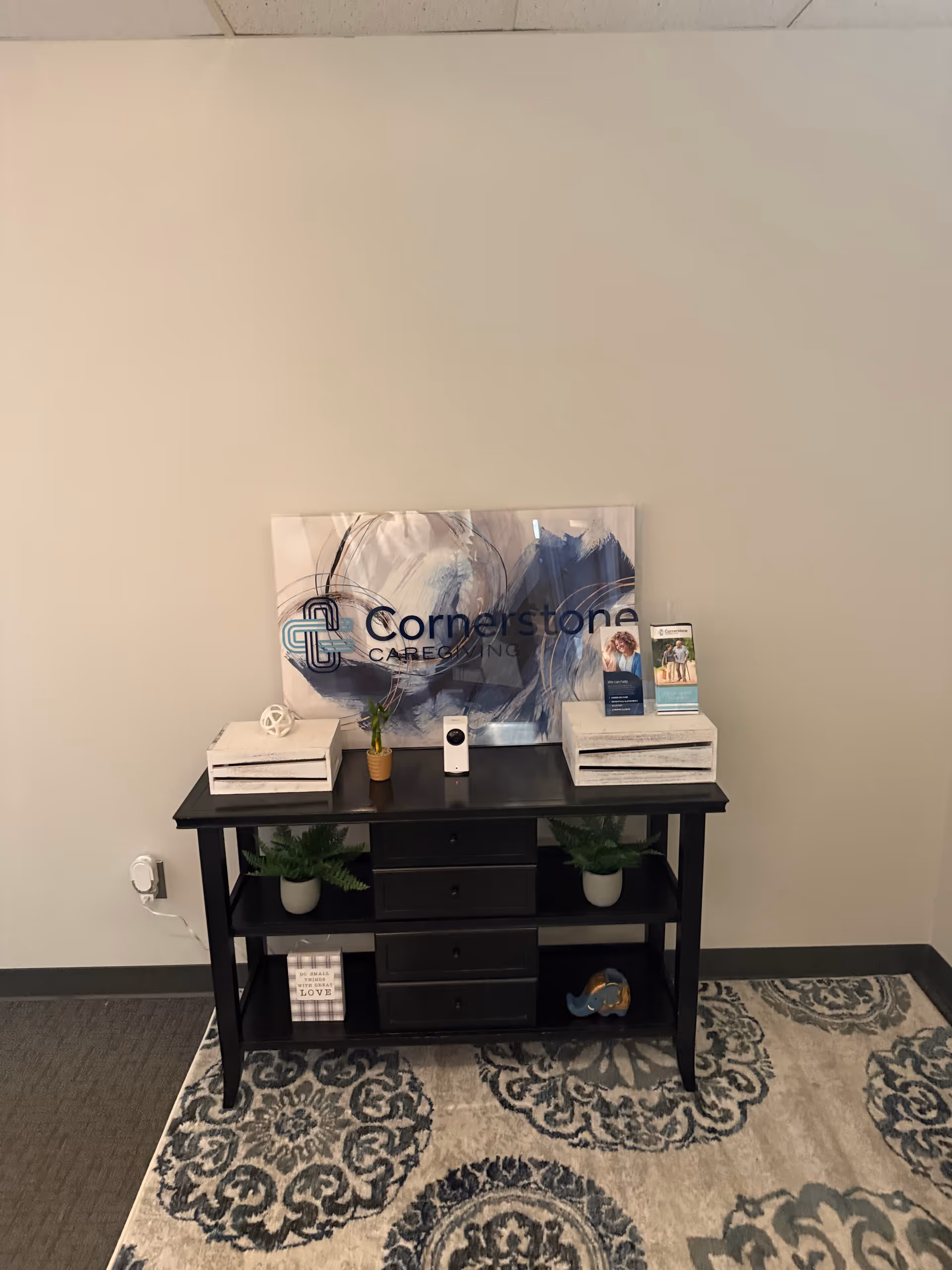 Reception area featuring Cornerstone Caregiving sign, black console table, plants, and brochure stands.