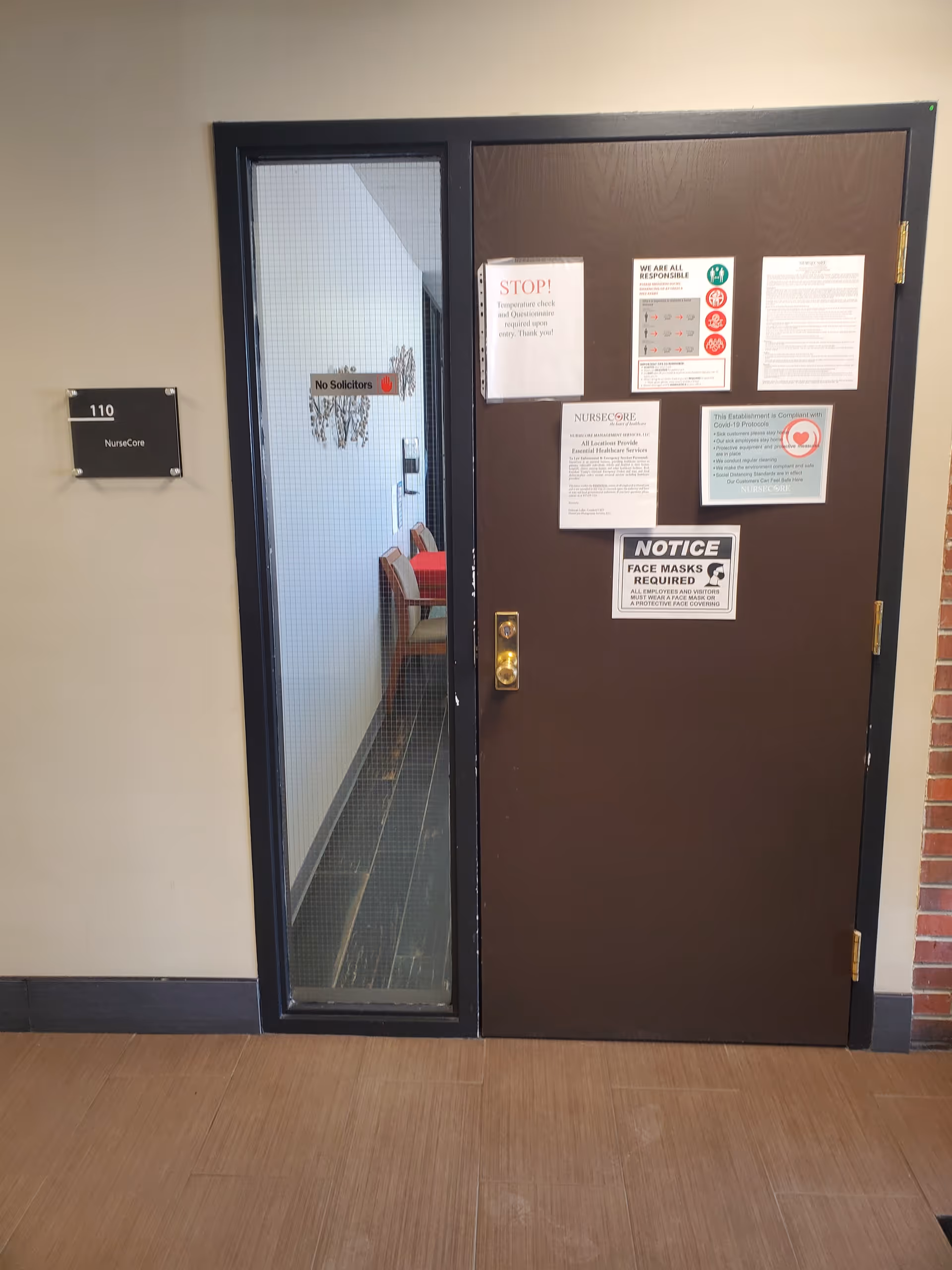 Brown entry door with NurseCore notices and glass panel in a hallway interior.