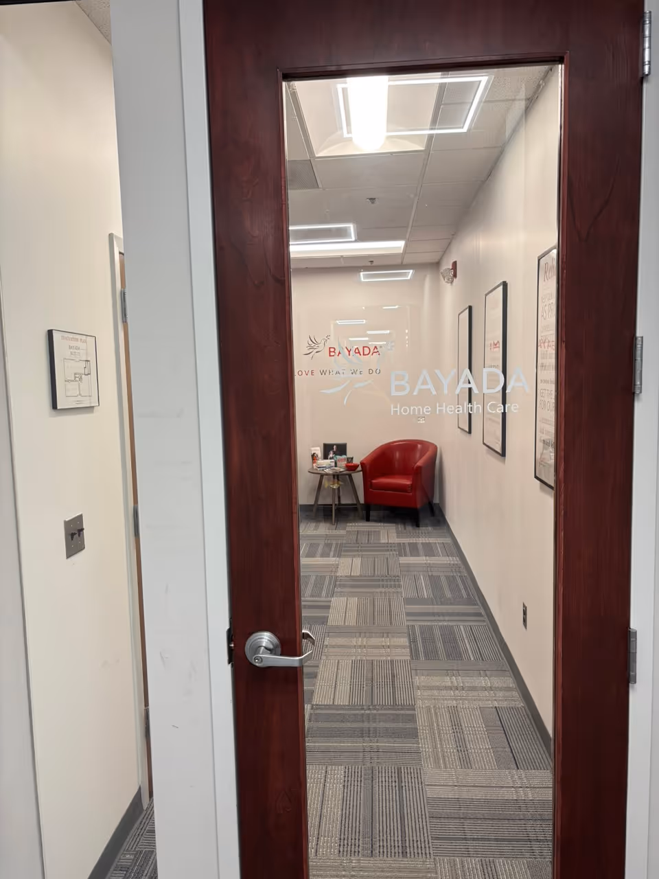 Doorway opens to a hallway with a red chair and Bayada Home Health Care sign.