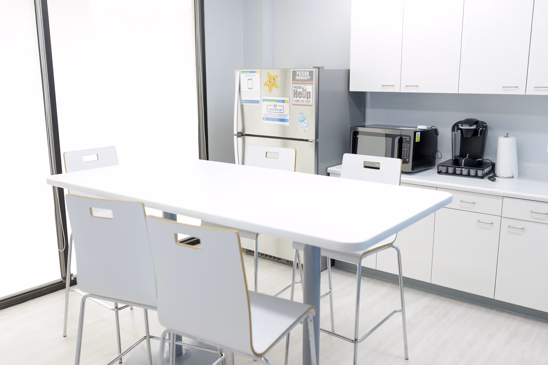 Bright white kitchenette in a senior living facility with a high table and appliances.