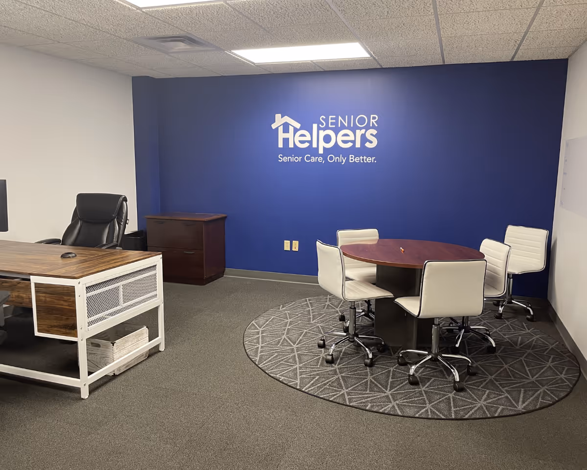 Office meeting area with blue wall displaying Senior Helpers logo and round table.