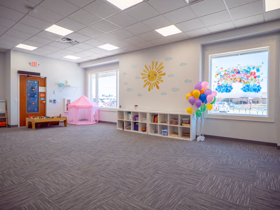 Bright playroom with cubby shelves, a pink tent, balloons, and sun wall mural.