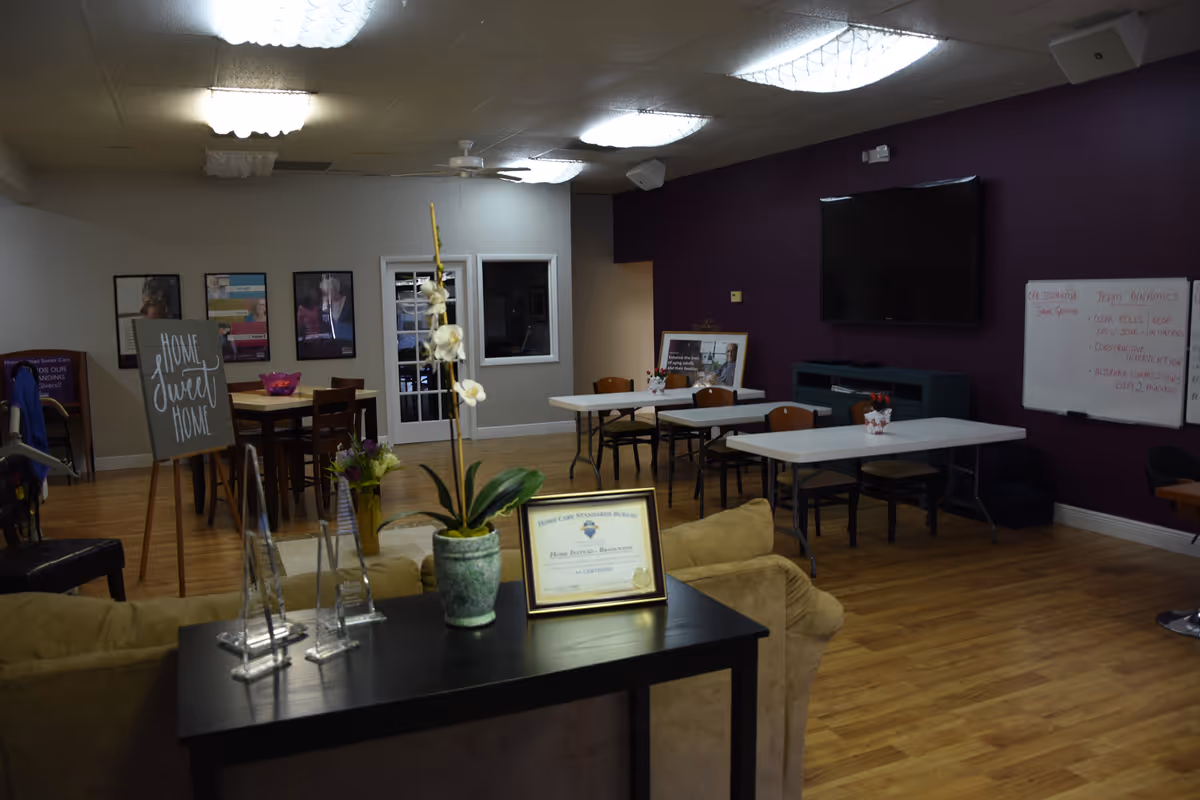 Indoor common area with tables, chairs, purple accent wall, TV, and certificate on table.