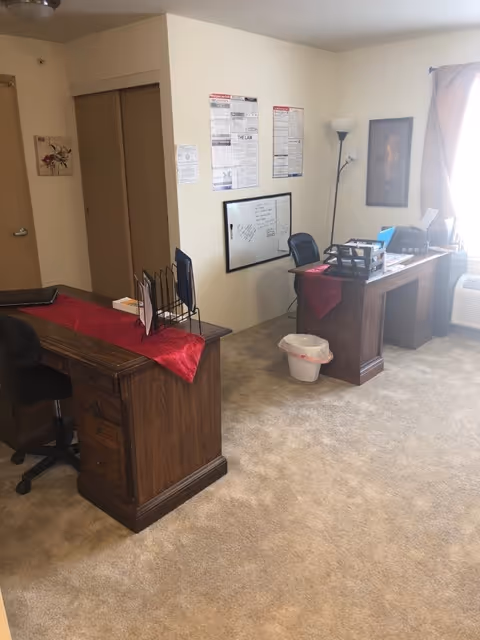 Interior reception area of a senior living facility with two desks and wall notices.