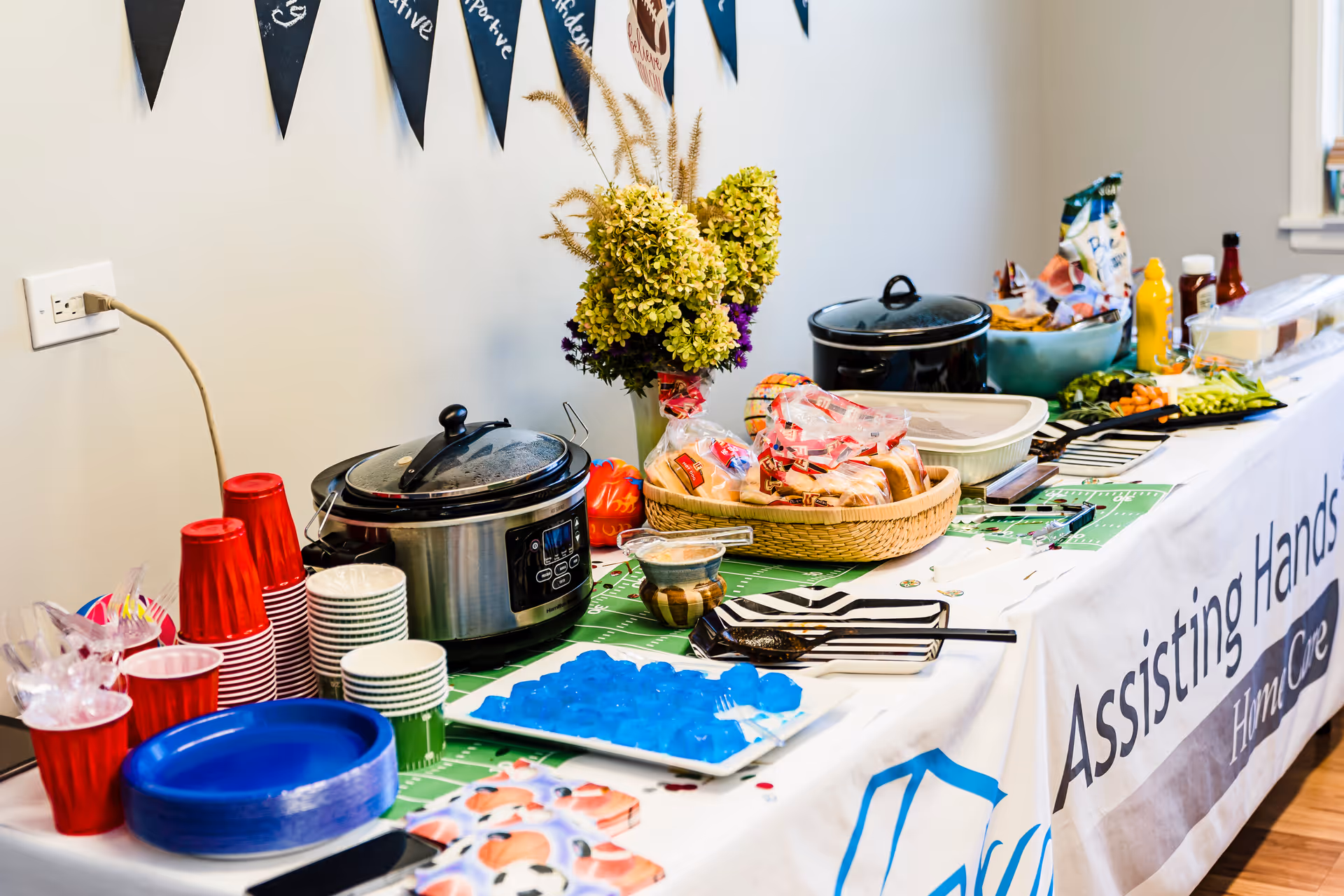 Indoors, a buffet table with food and a banner reading Assisting Hands Home Care.