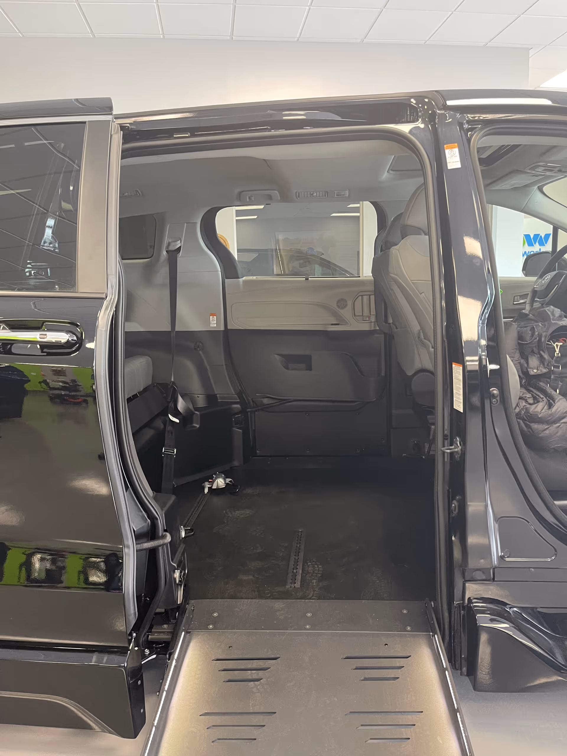 Inside a MobilityWorks showroom, a black accessible van with a lowered ramp and open doors.