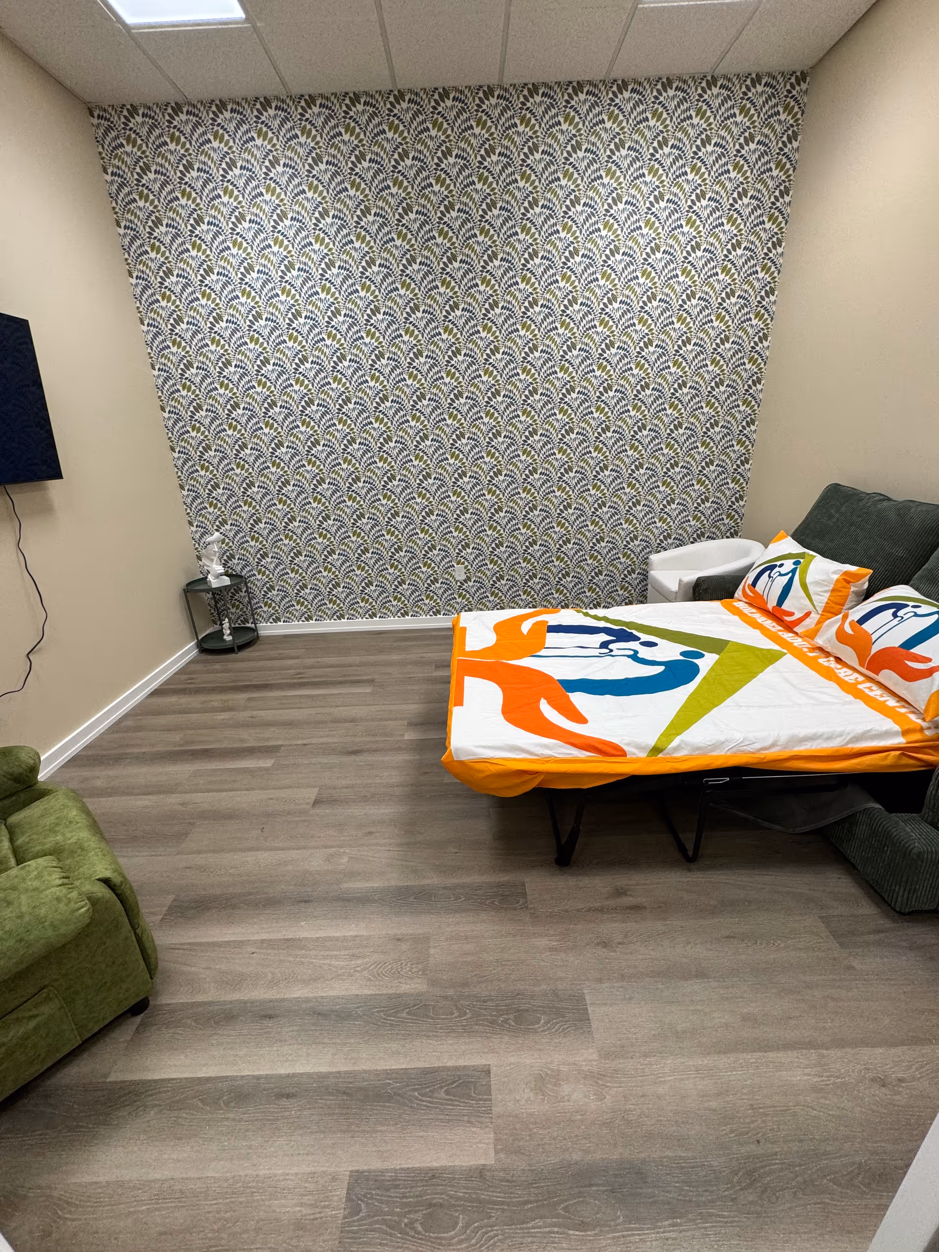 Small bedroom in a senior care center with a colorful bedspread and patterned accent wall.
