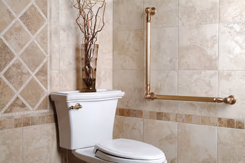 White toilet with bronze grab bar and vase on beige tiled bathroom wall.