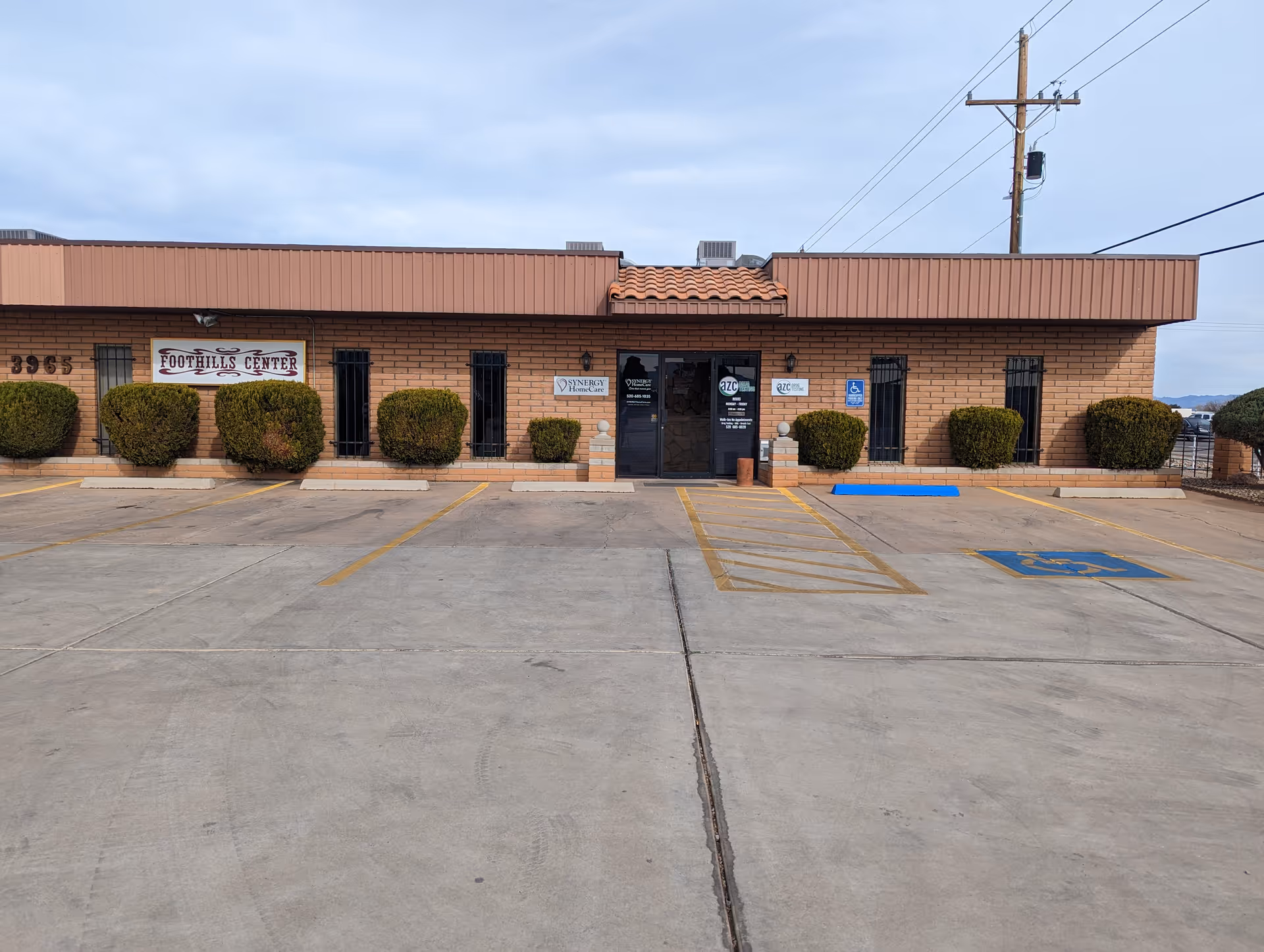 Front exterior of a brick facility with shrubs, glass entrance, and a parking lot.