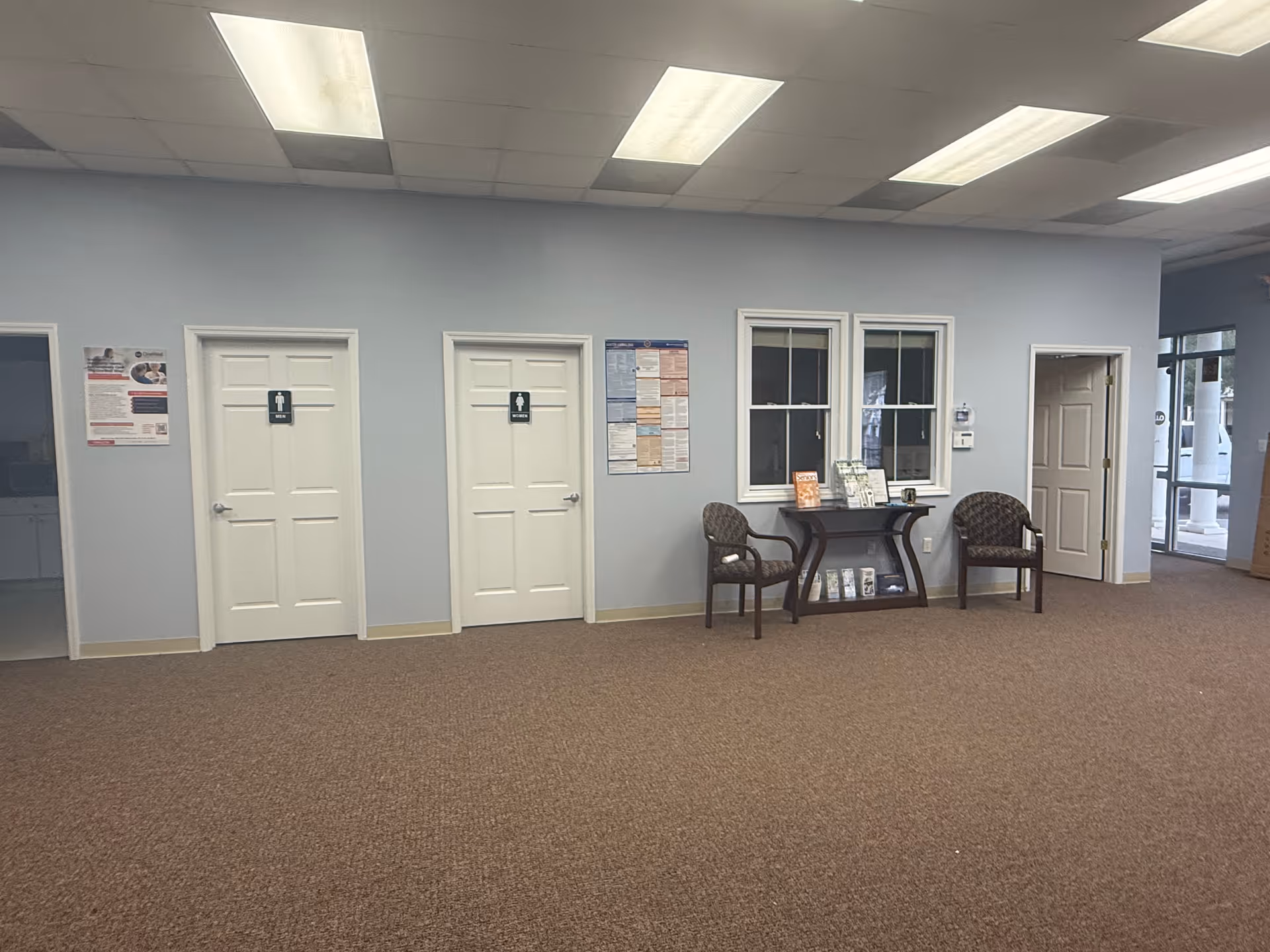 Light blue interior lobby with doors, a window, and two chairs beside a small table.