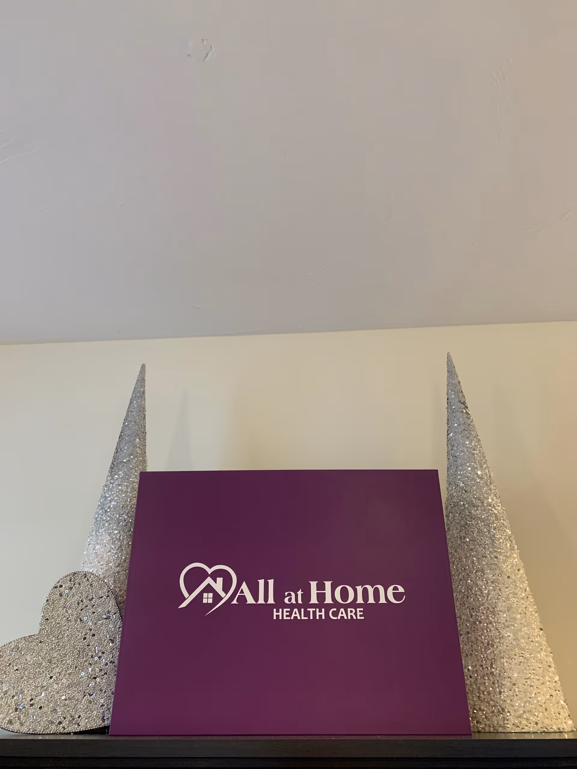 Purple All at Home Health Care sign flanked by glittery cone decorations on a shelf.