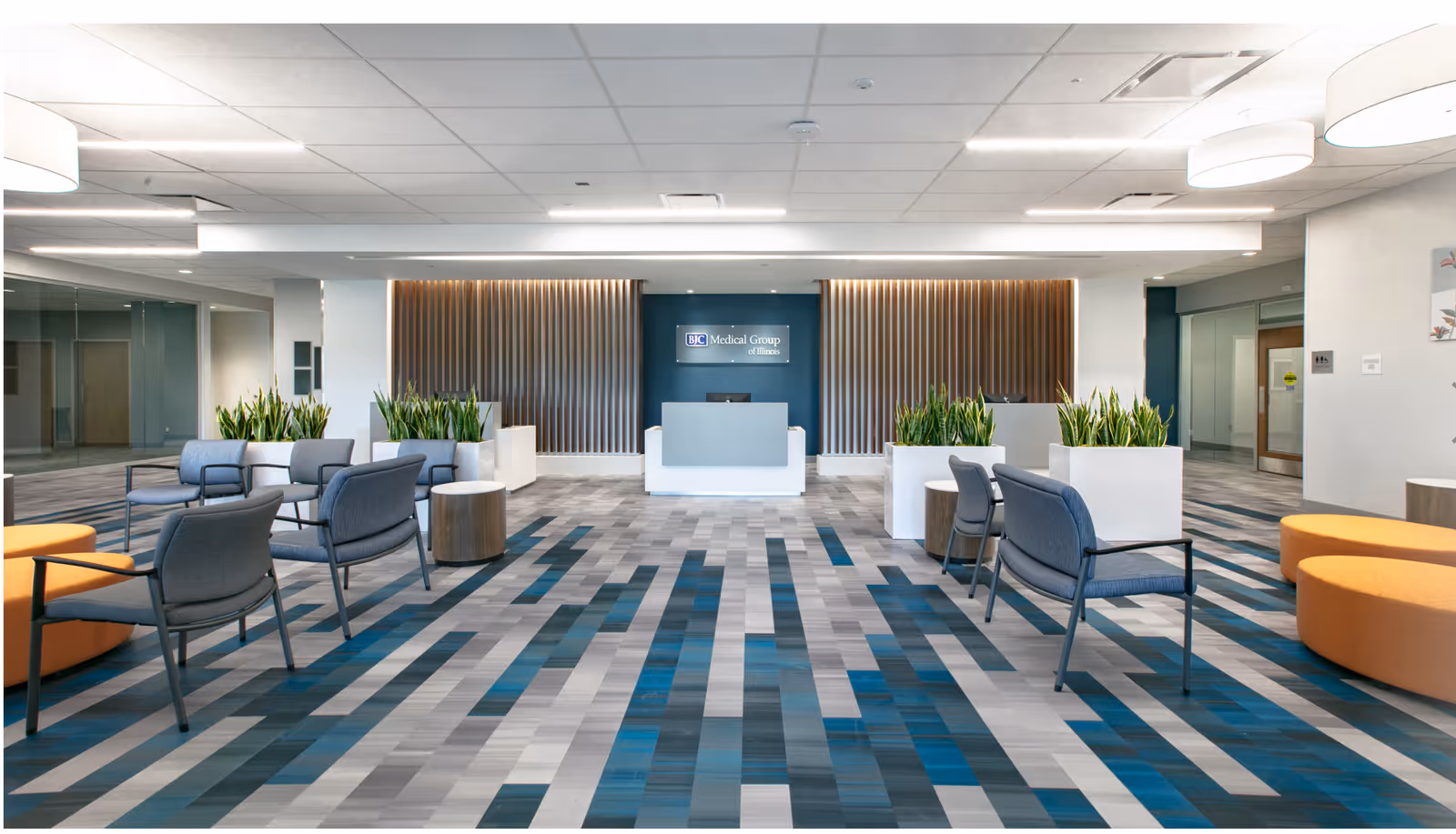 Modern hospital lobby with seating, plants, and a central reception desk.