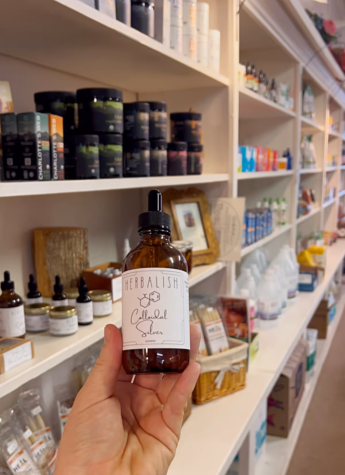 Hand holds herbal bottle in a white-shelved aisle of wellness products.