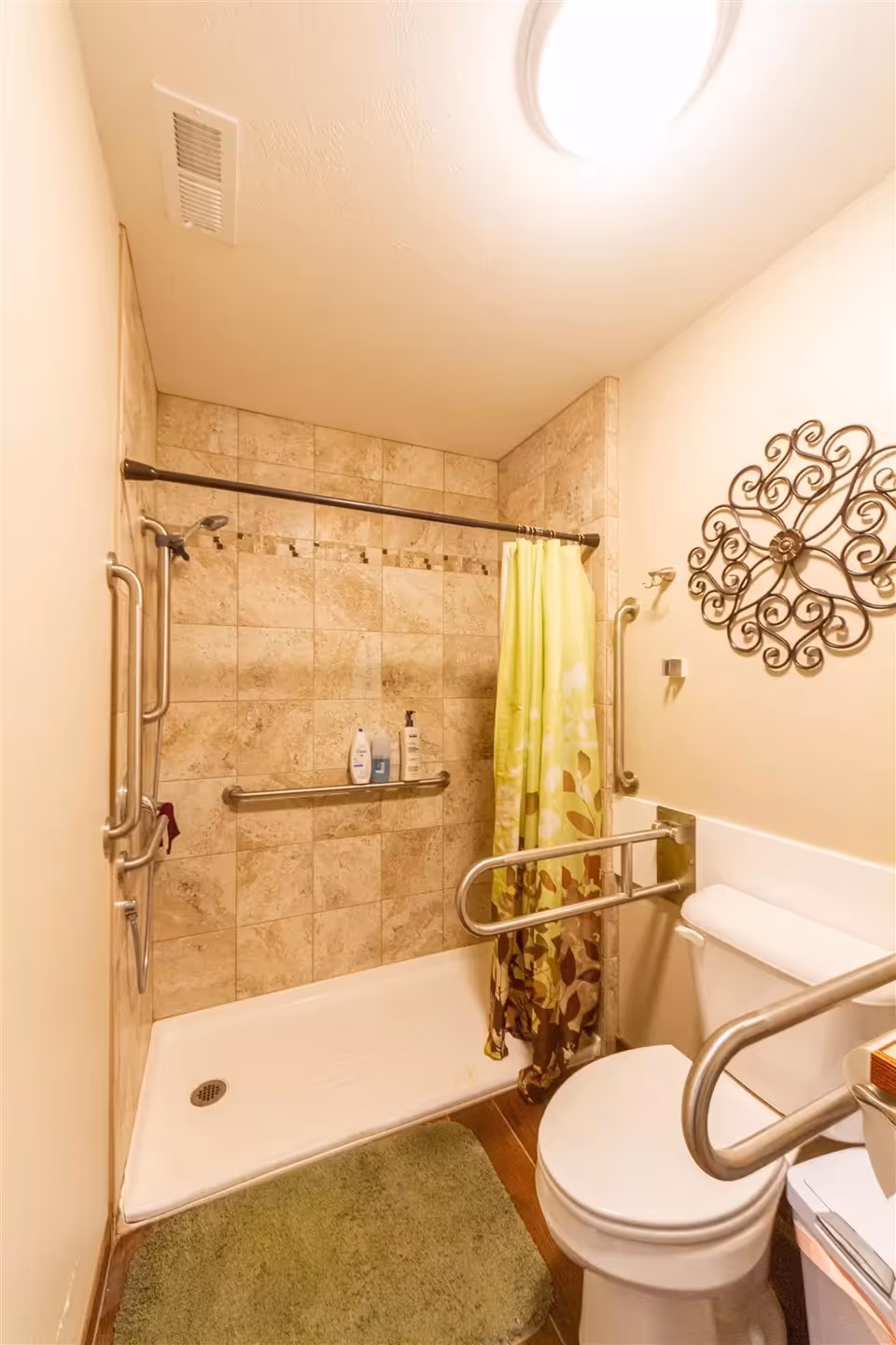 Small tiled bathroom featuring a walk-in shower, metal grab bars, and a toilet.