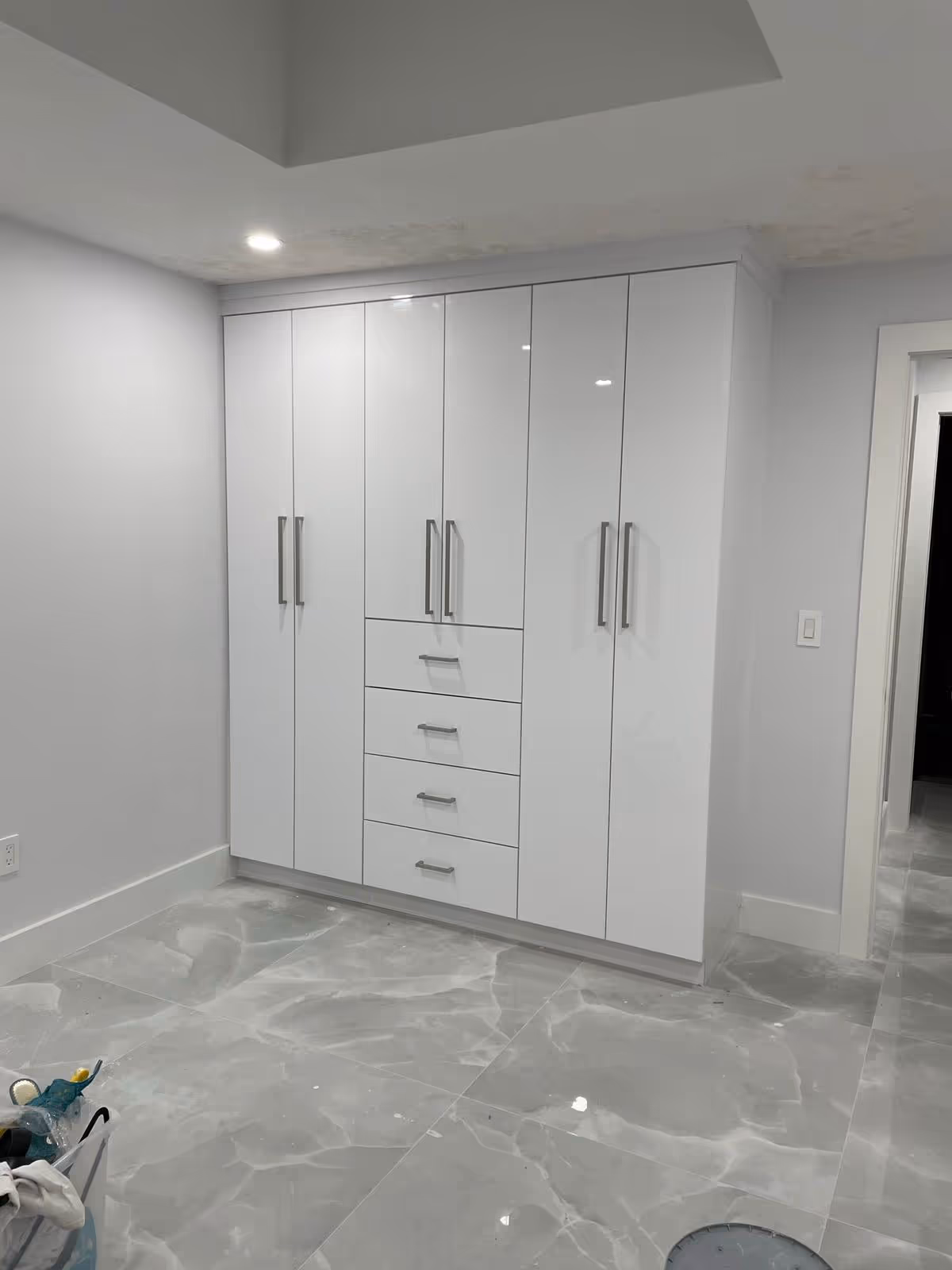 White built-in wardrobe with multiple doors and drawers against light gray walls.