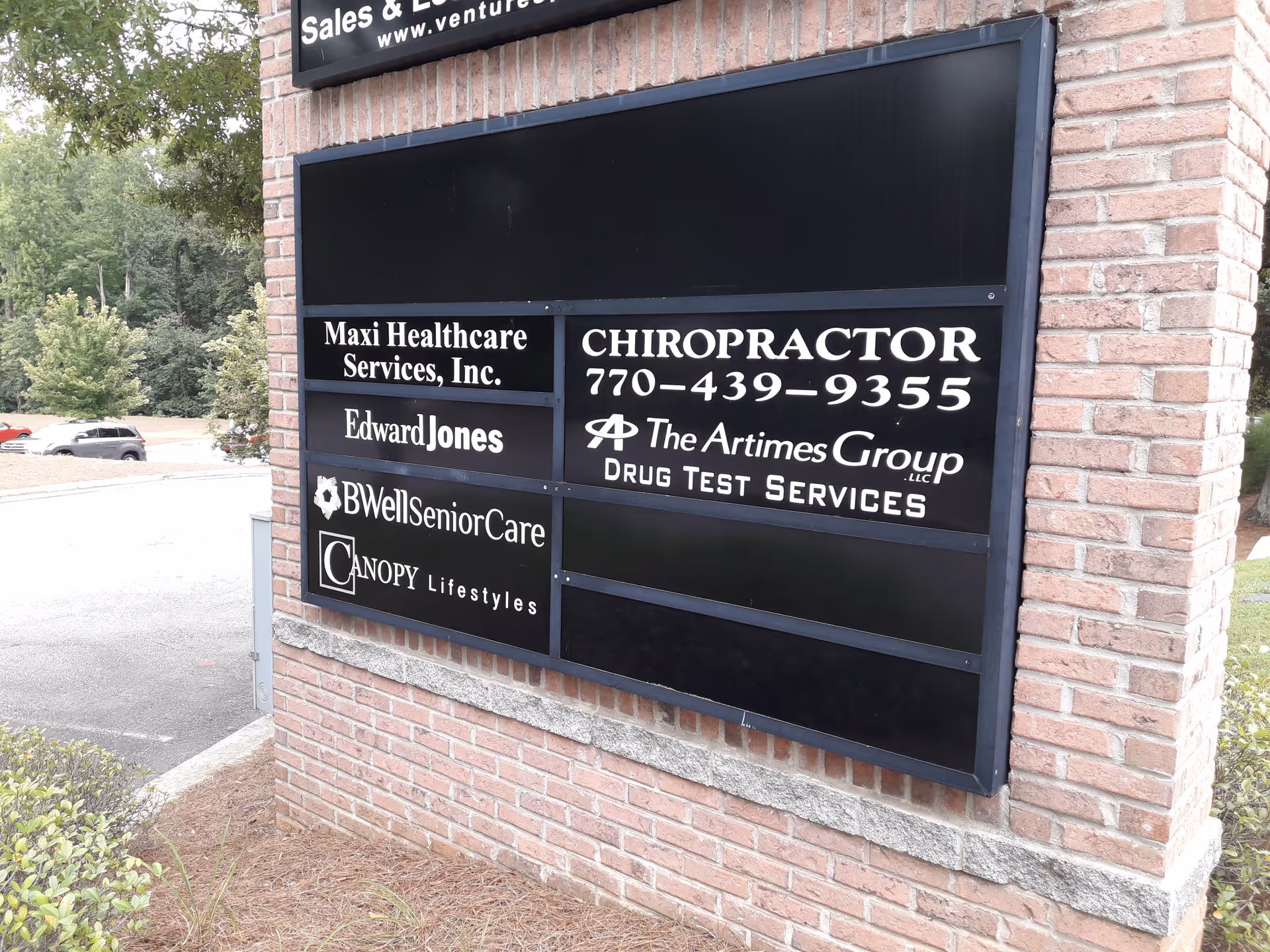 Exterior brick sign board displaying Maxi Healthcare Services and other business names.