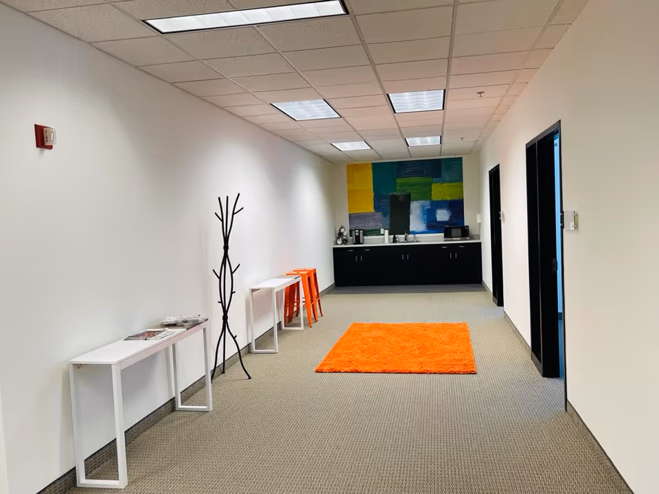 A bright hallway with white walls, an orange rug, and a kitchenette at the far end.