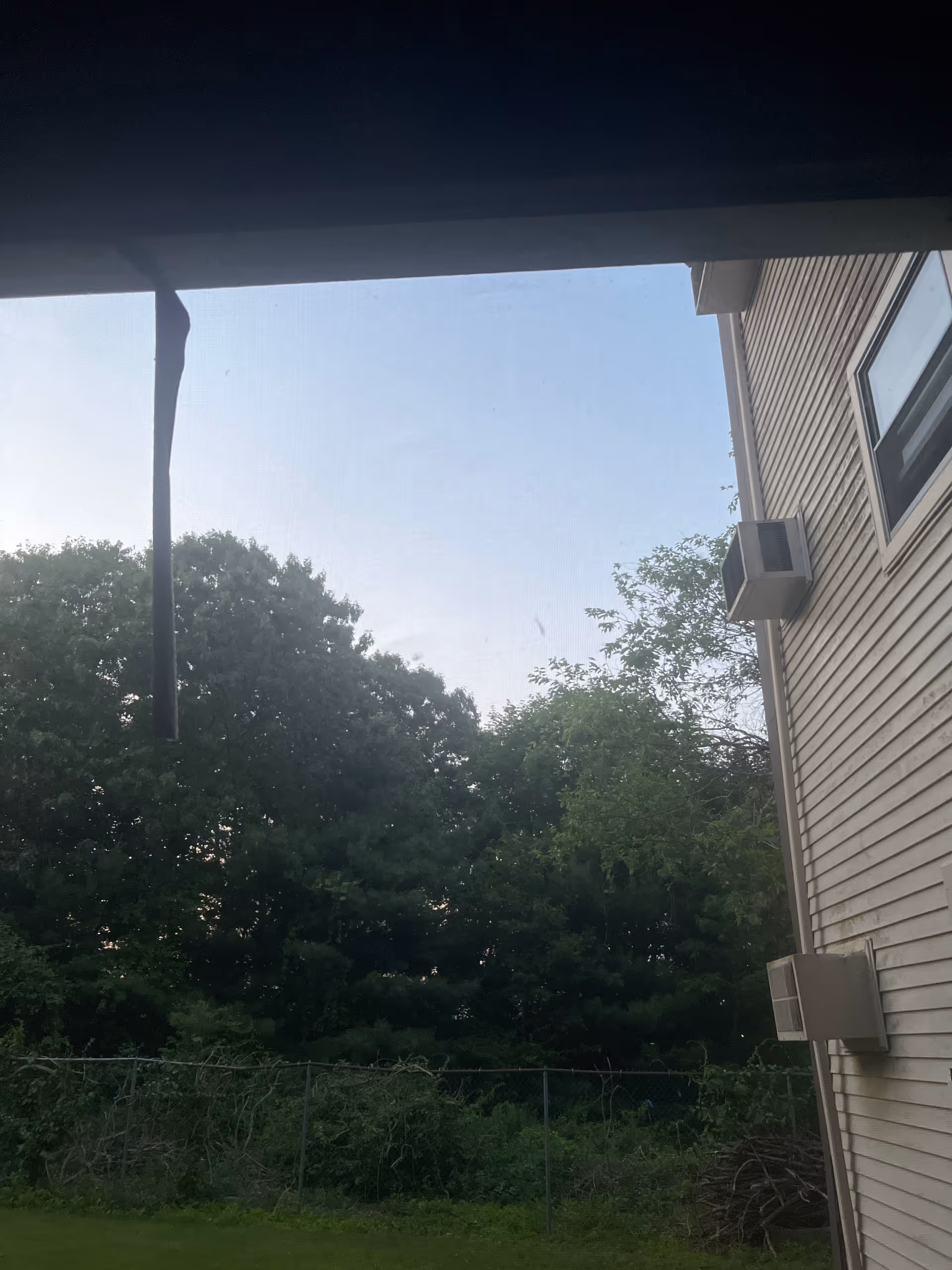 Outdoor view of building exterior with an air conditioner, fence, and trees.