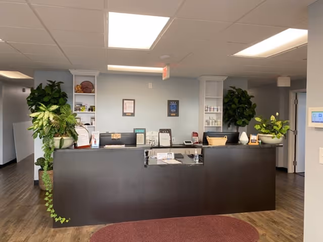 A modern reception area at Balanced Physical Therapy with plants, shelves, and a dark front desk.