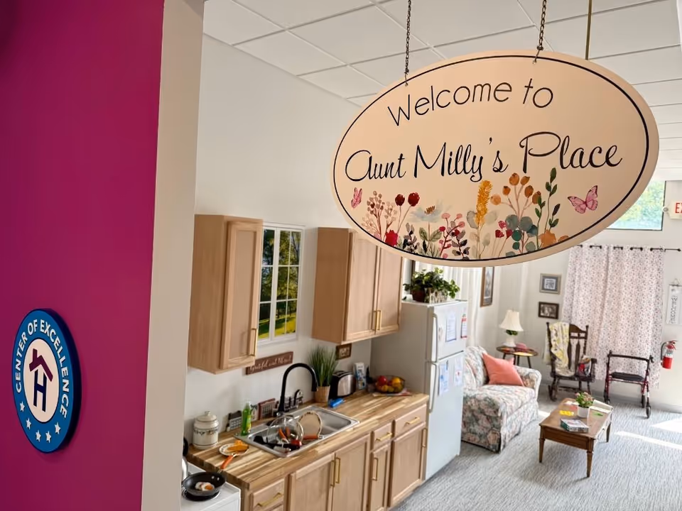Interior of a senior living space with a hanging Welcome sign and small kitchenette.