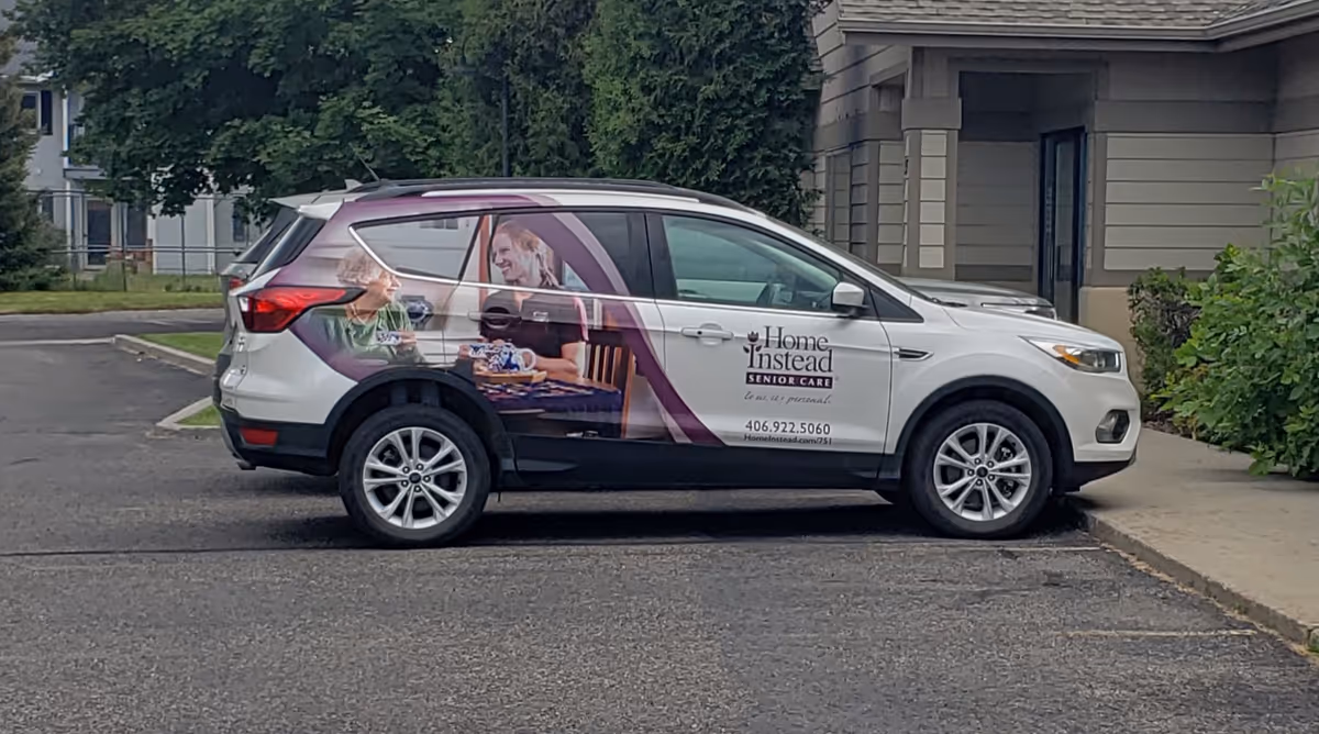 A Home Instead branded vehicle parked in a lot beside a senior living facility.