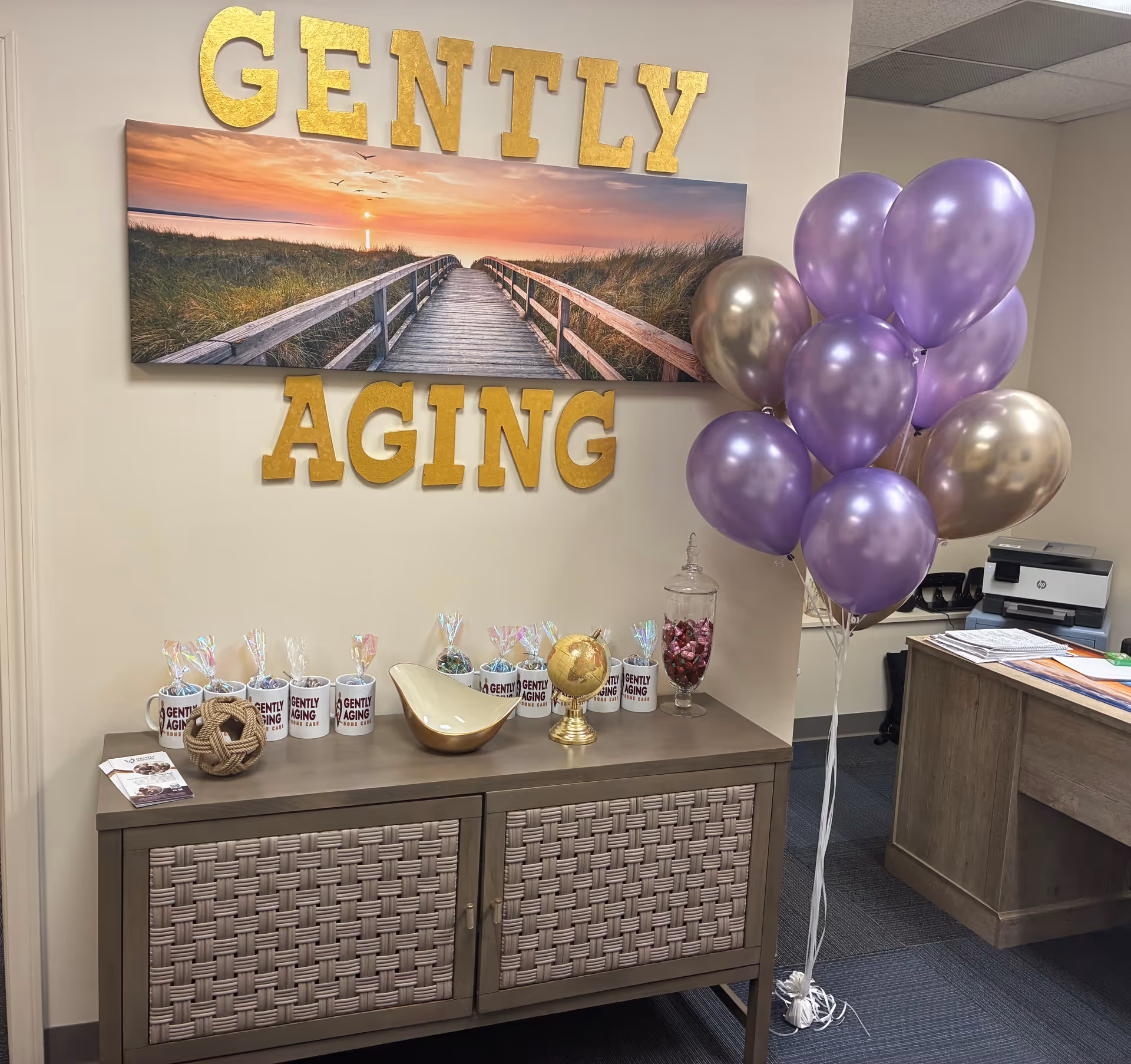 Reception area with wall sign 'GENTLY AGING', sunset artwork, purple balloons, and a console table.