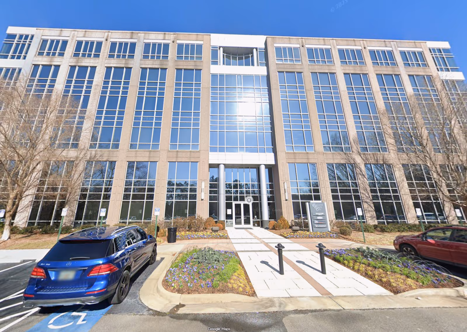 Modern glass-front building with central entrance and landscaped walkway in front.