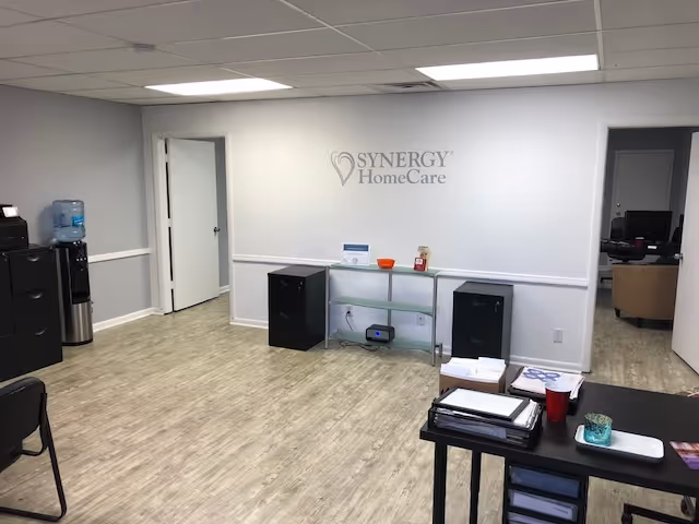 Interior reception area with Synergy HomeCare logo, office furniture, and a desk.