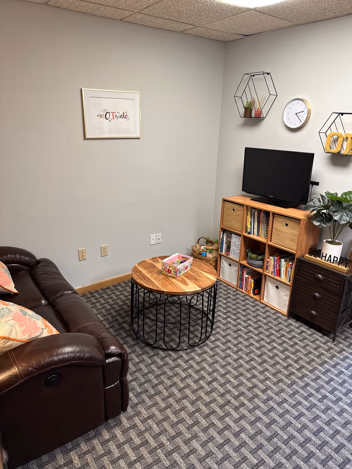 Cozy interior lounge in a senior facility with leather sofa, wooden shelves, and TV.