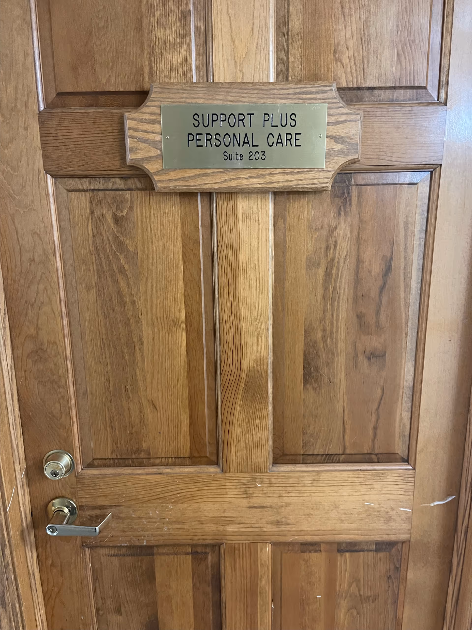 Wooden interior door with brass sign reading Support Plus Personal Care, Suite 203