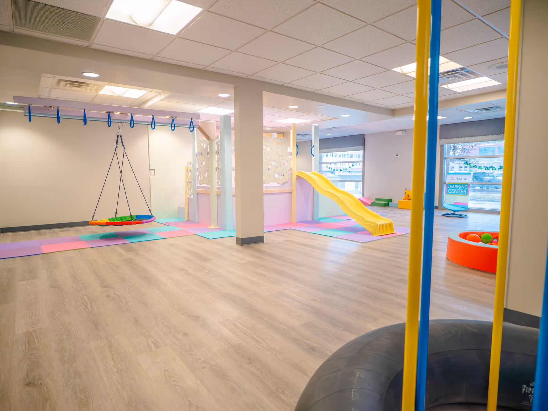 Bright indoor play area with a yellow slide, swing, and colorful soft mats.