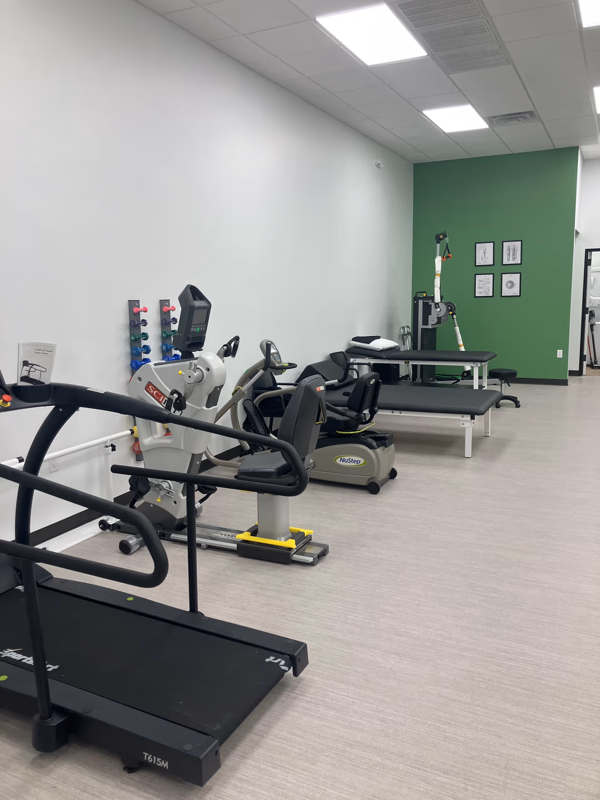 Empty rehabilitation gym with treadmills, stationary bikes, and therapy equipment in a bright room.