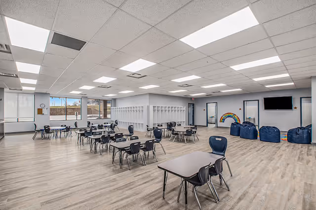 Spacious indoor community room with tables, chairs, cubbies, and blue bean bags.